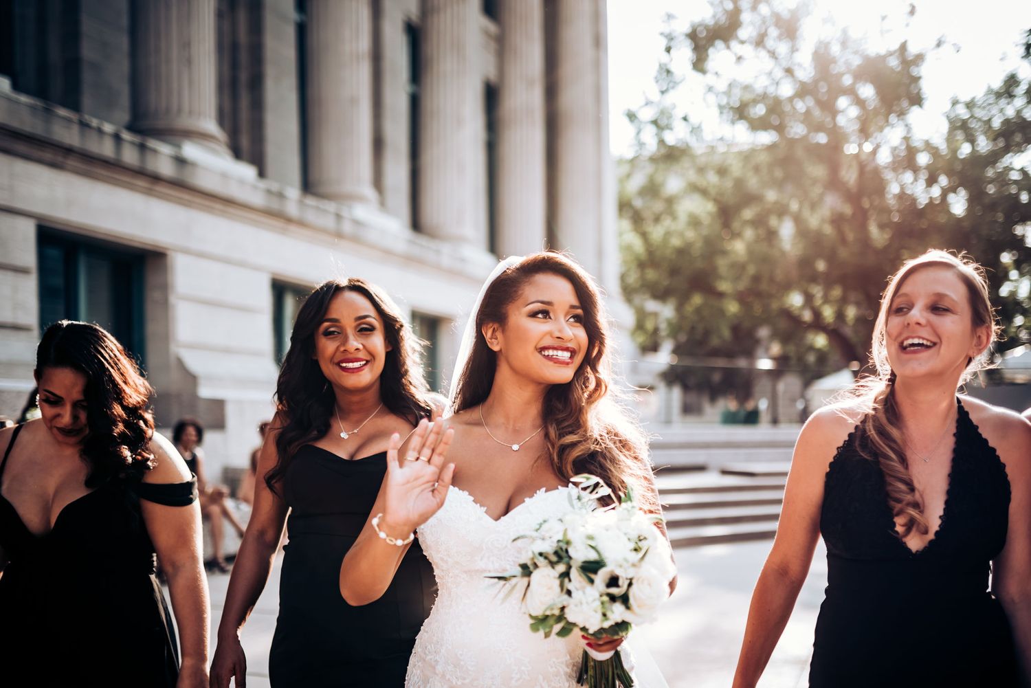 Candid moment of bridal party sharing laughter while walking outside elegant building.