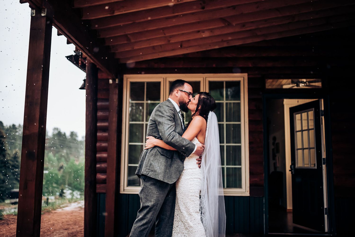 Romantic outdoor portrait of newlyweds sharing tender moment against rustic cabin backdrop.