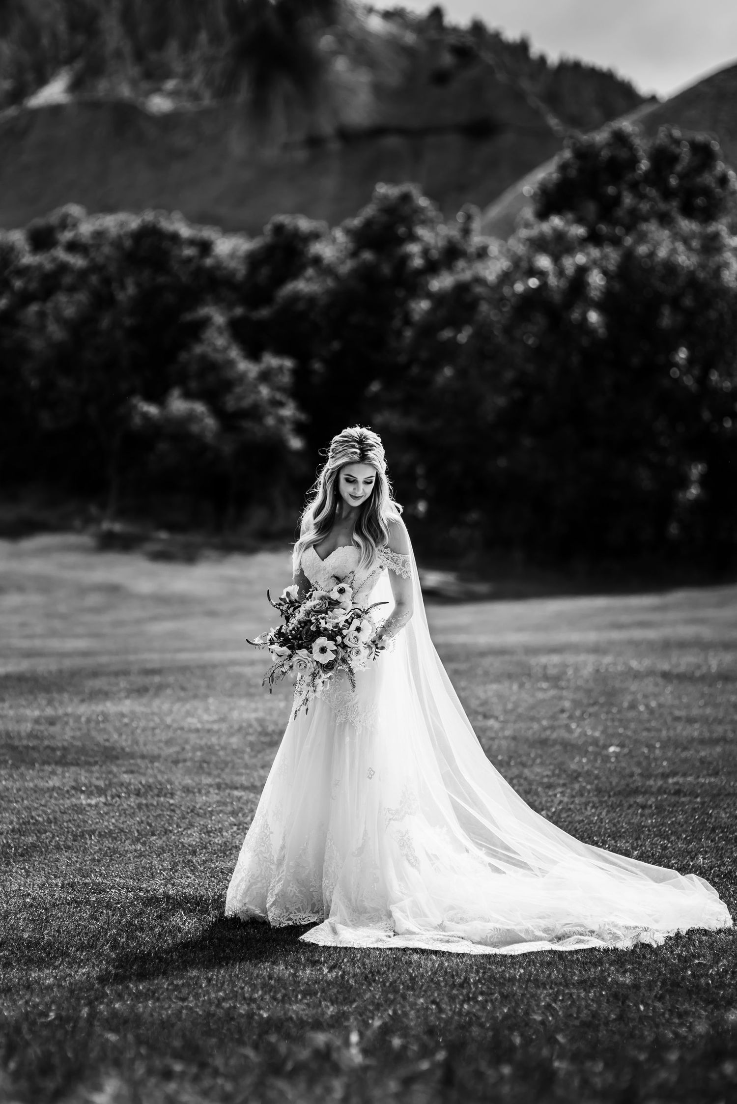 Bride in flowing white gown poses in mountain meadow in dramatic black and white.