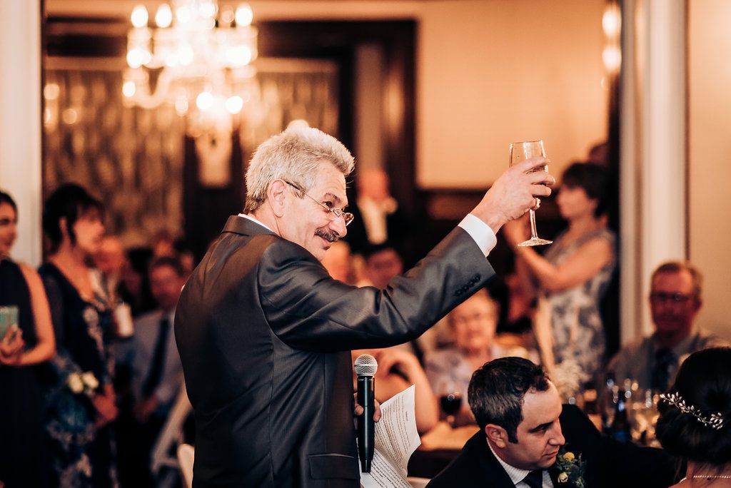 Guest giving animated wedding toast with raised glass at reception dinner.