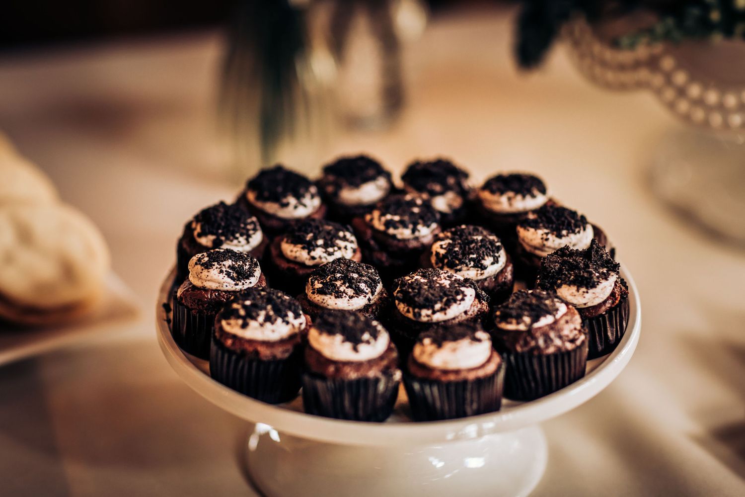 Chocolate cupcakes with dark frosting arranged on white pedestal plate.