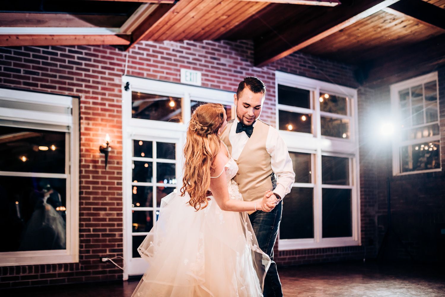 Couple shares an intimate slow dance in an elegantly lit brick venue.