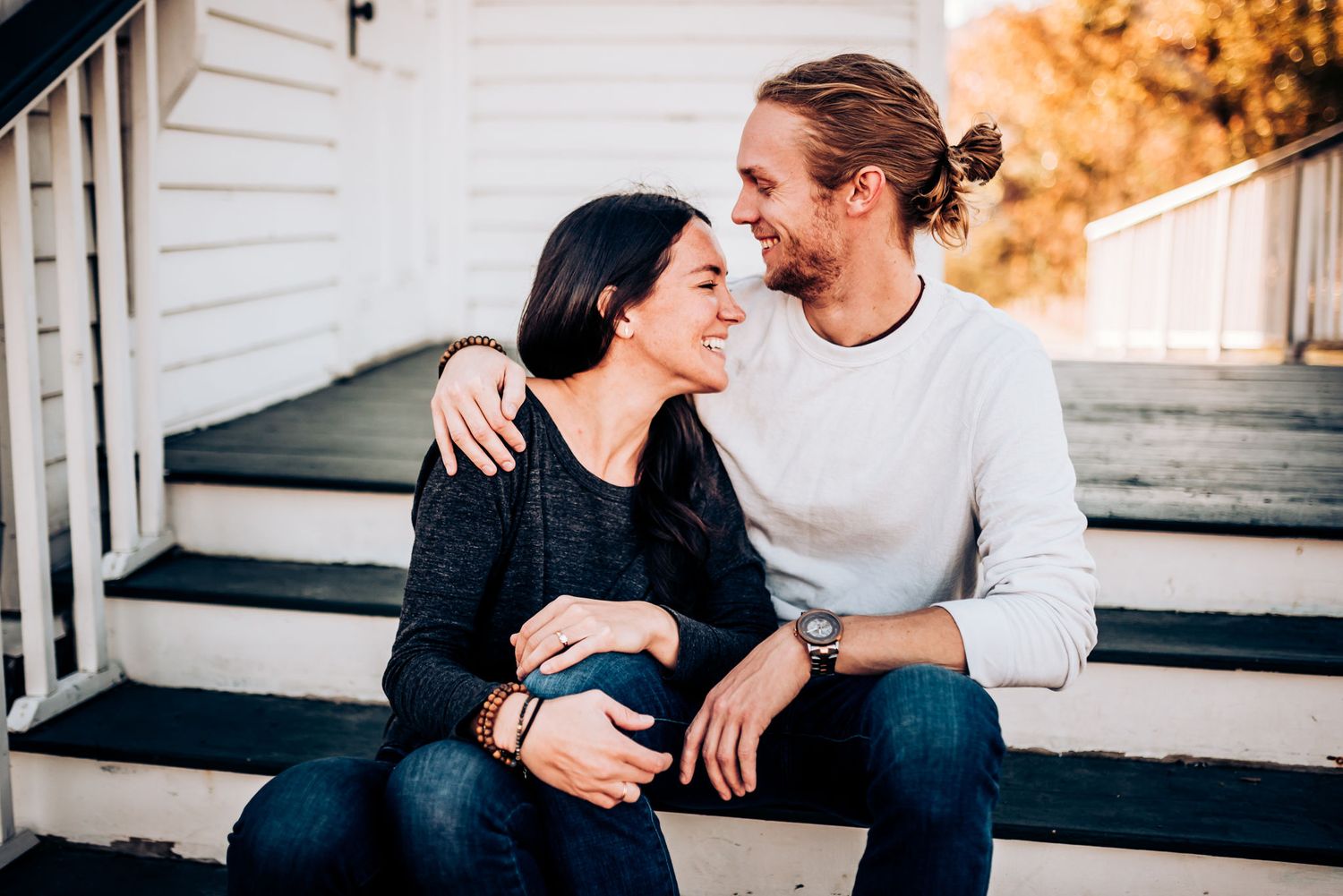 Couple sharing tender moment while sitting on white porch steps.