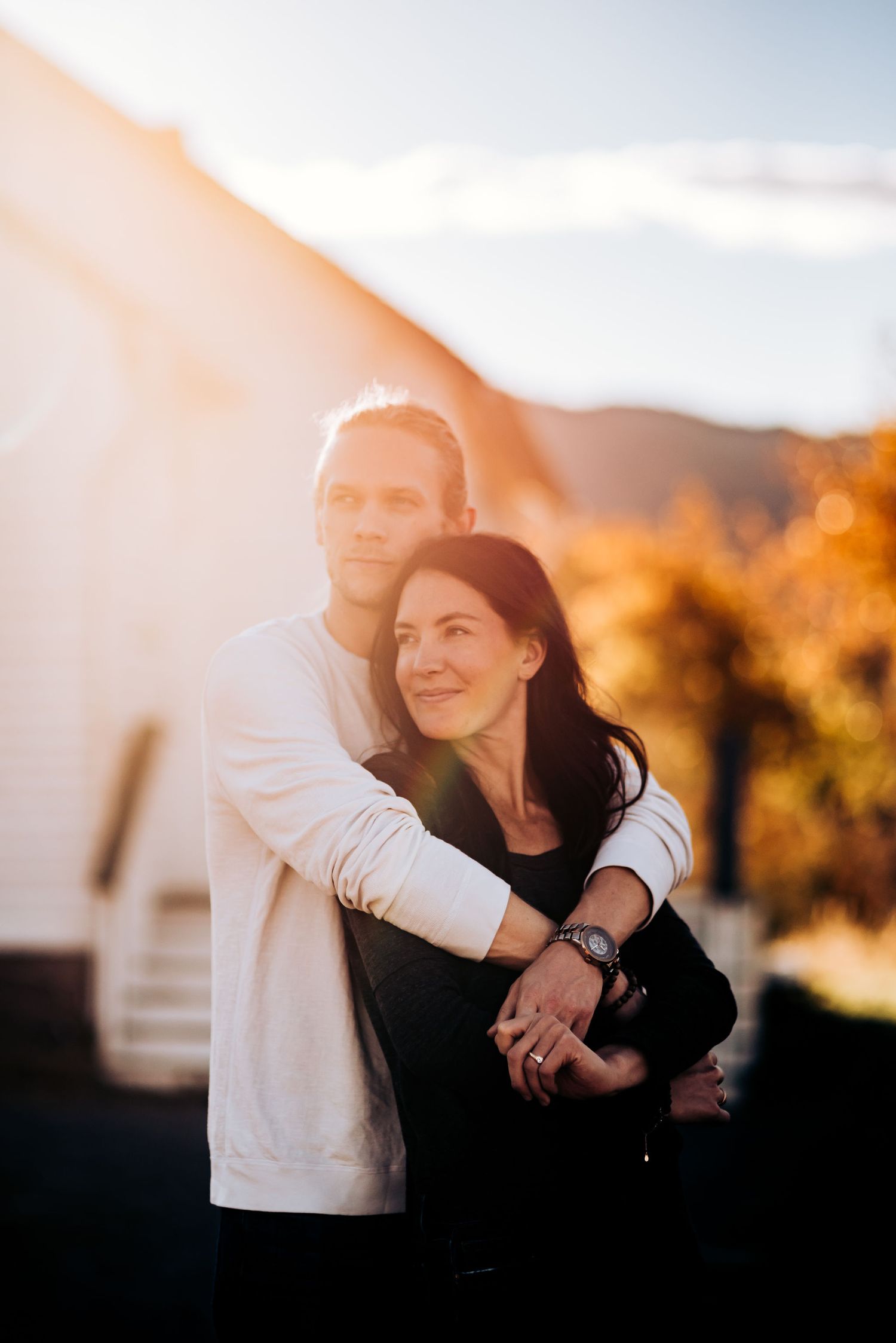 A romantic embrace outside a white building during sunset with mountains visible in the distance.