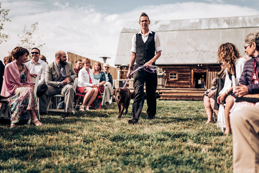 Outdoor wedding gathering with guests seated on lawn chairs facing a speaker.