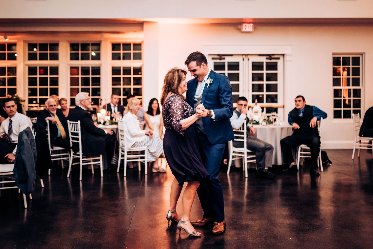 Couple dances together on the reception floor while guests watch from decorated tables.