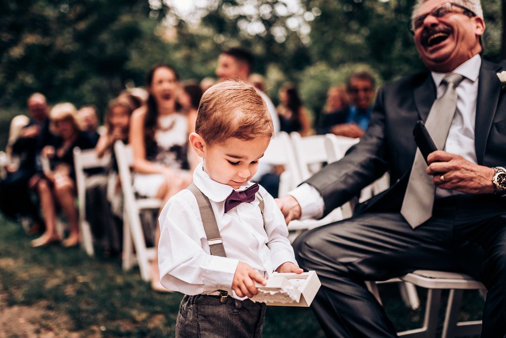 Heartwarming interaction between formal-dressed guest and young attendant at outdoor wedding.