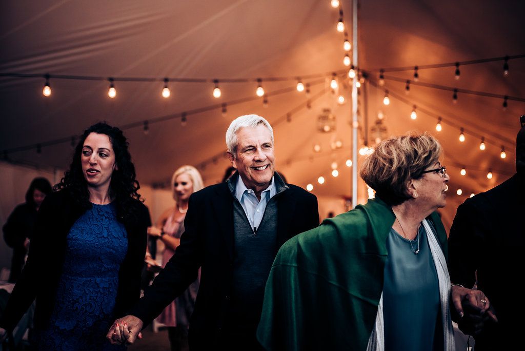Wedding guests dancing and celebrating under warm tent lighting.