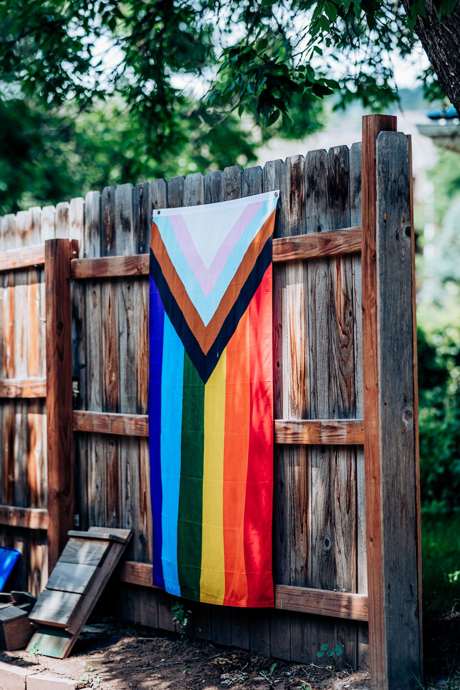 Rainbow pride flag with chevron design hanging on a rustic wooden fence.