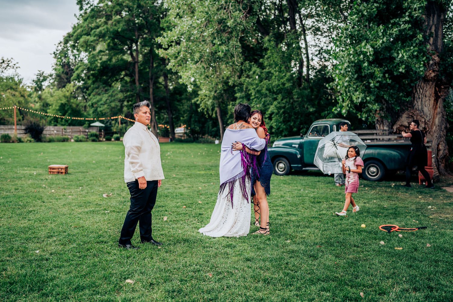 Small gathering on a green lawn with trees and a vintage car in the background.