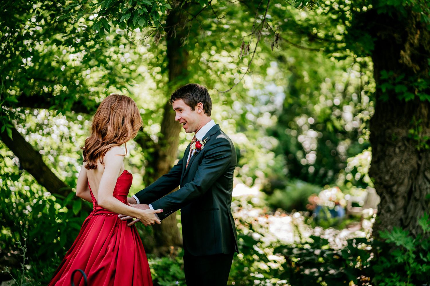 Romantic moment between couple in red dress and black suit among green garden foliage.