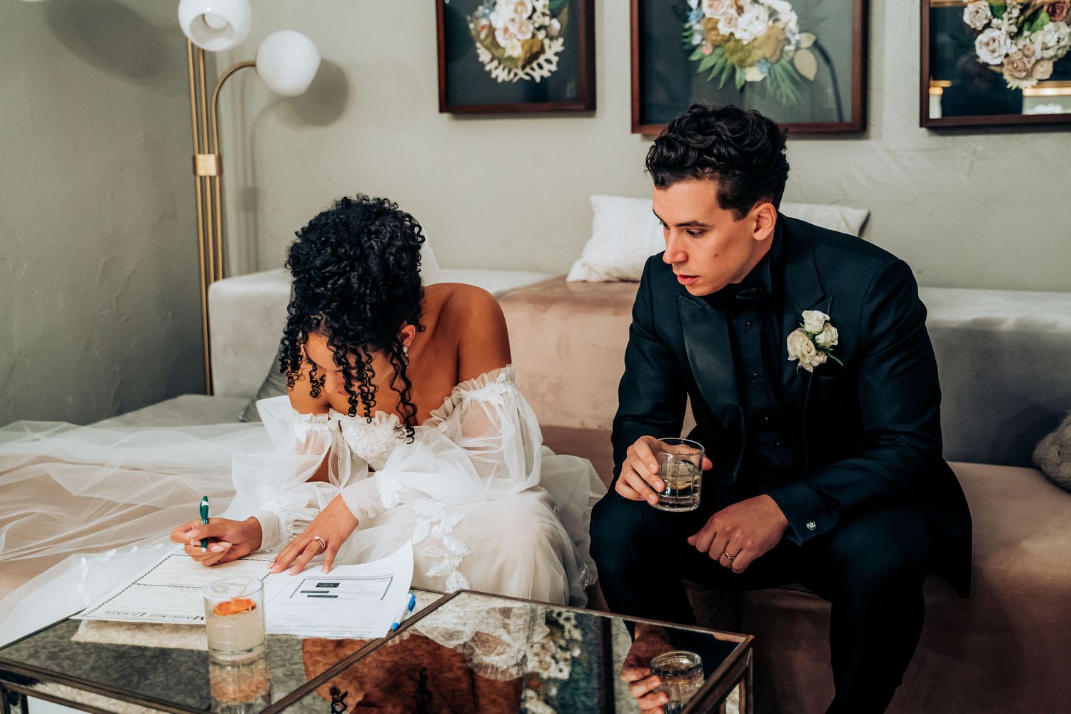 Couple signing wedding documents together on a couch while enjoying drinks in an intimate setting.