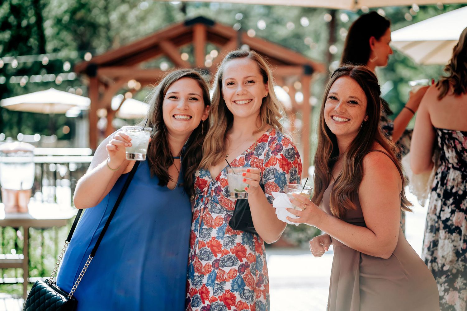 Three wedding guests enjoying drinks and conversation at outdoor mountain venue.