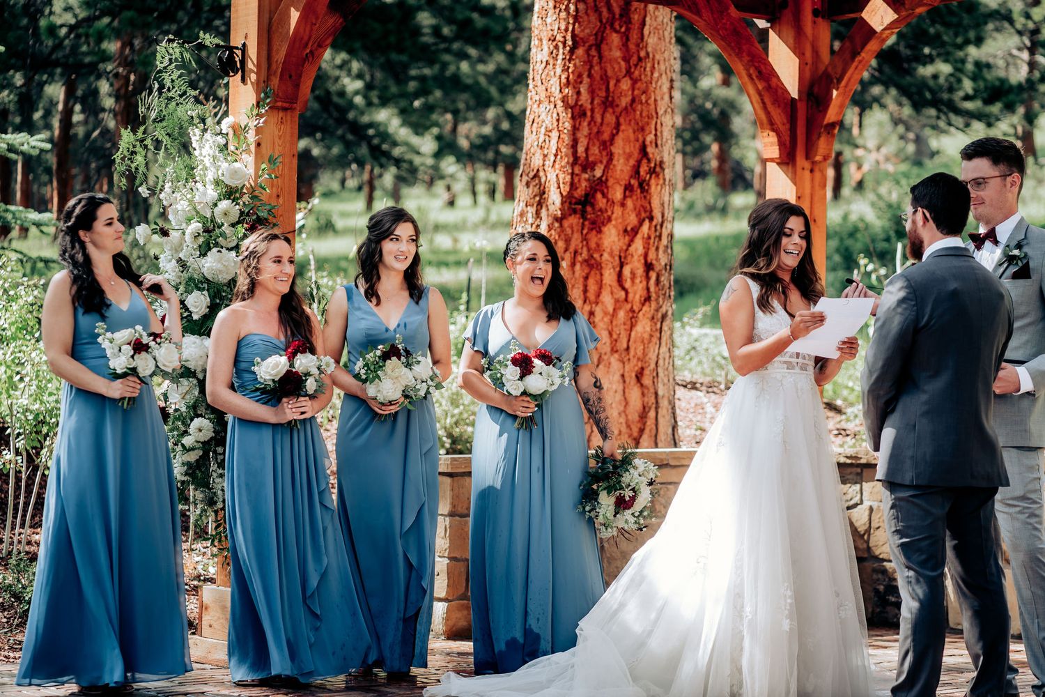 A wedding ceremony under wooden beams with bridesmaids in blue dresses.