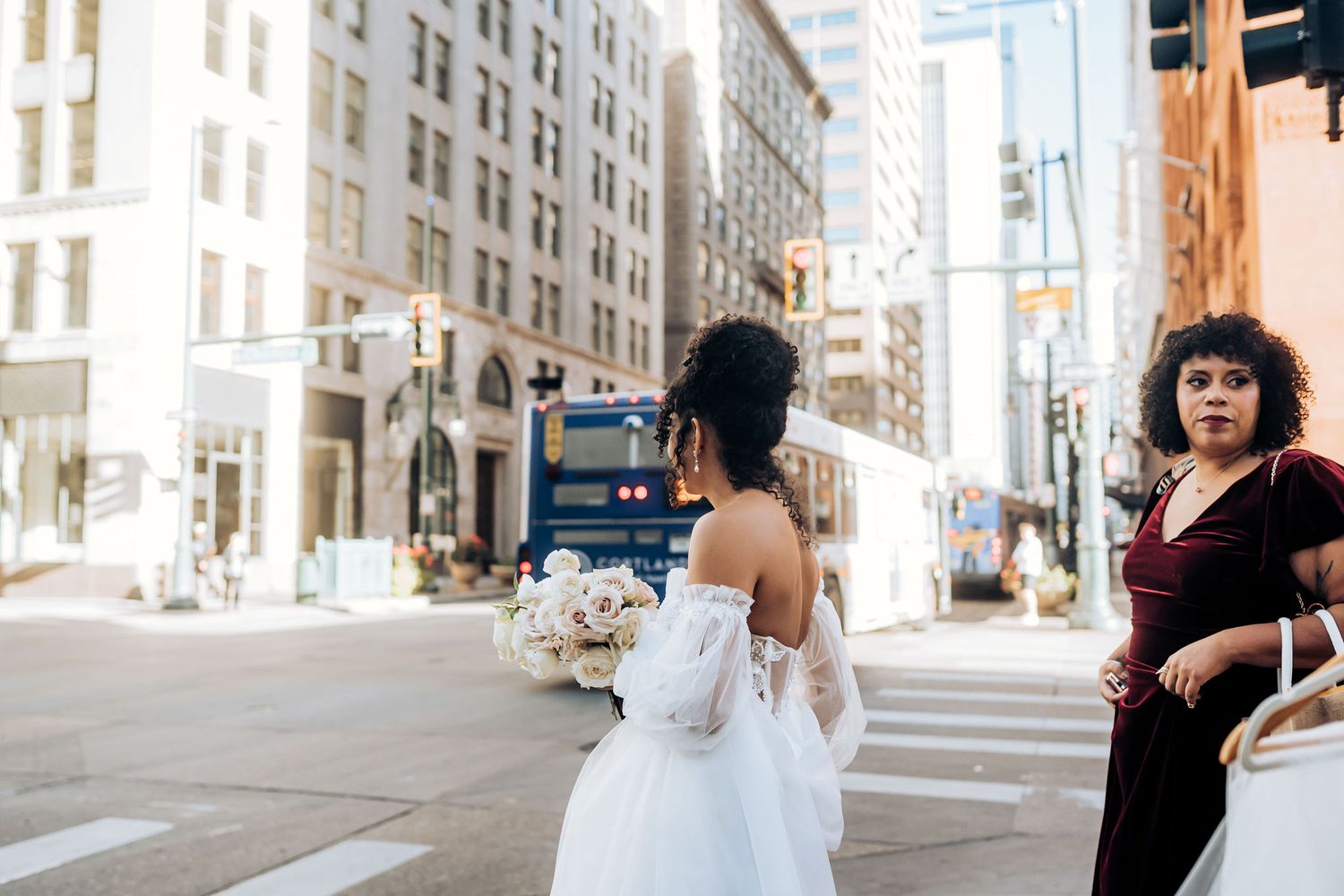 A bride in a white gown walks through city streets on her wedding day.