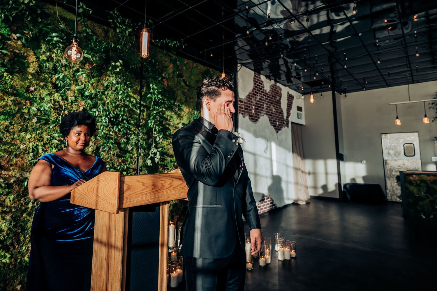 Wedding ceremony setting with modern industrial decor and lush greenery wall.