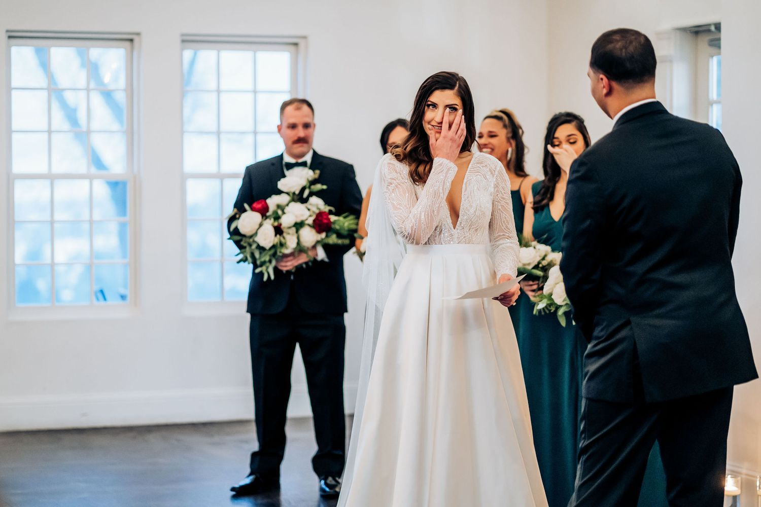 An emotional moment during a wedding ceremony in a bright white room with large windows.