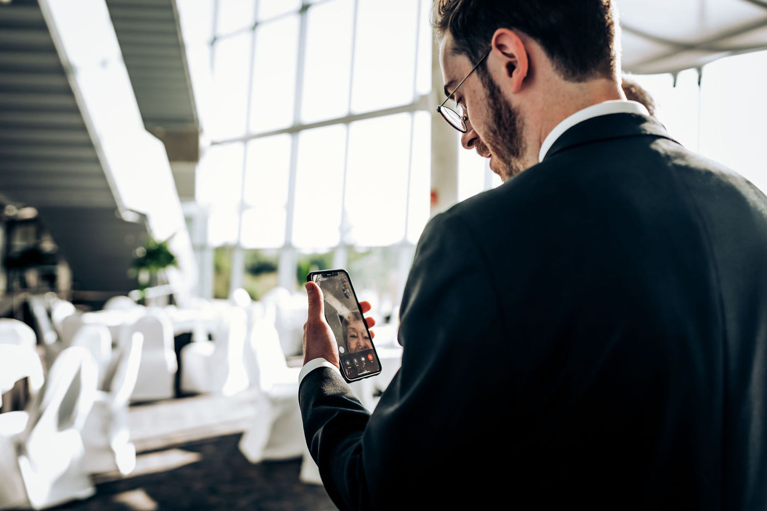 Business professional in a suit checks his smartphone in a brightly lit office space.