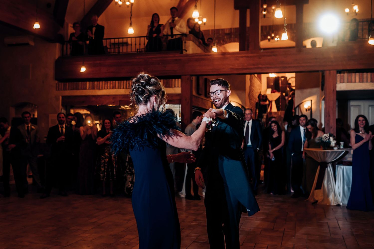 A couple performs a dance during a formal event in a warmly lit ballroom venue.