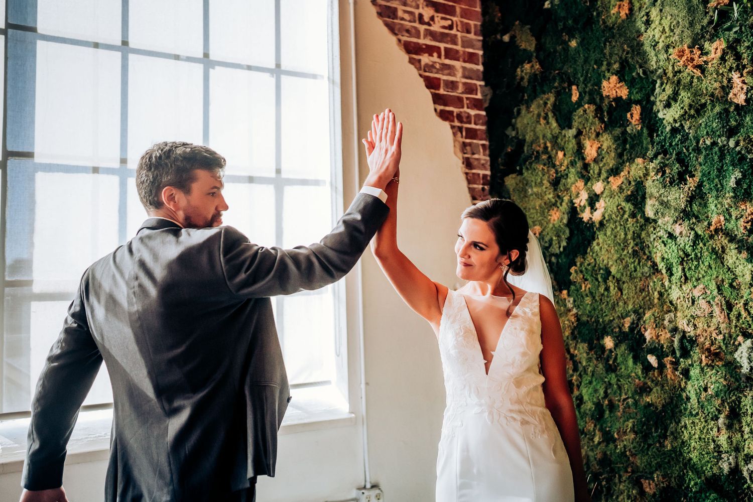 Wedding couple giving each other a celebratory high-five in an industrial-style venue.