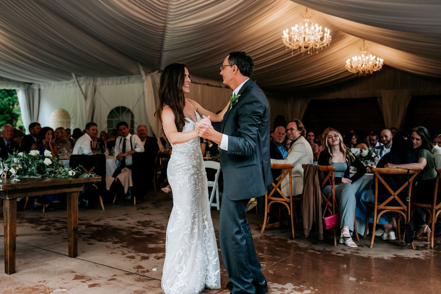 A couple shares their first dance in a draped tent reception with guests watching.