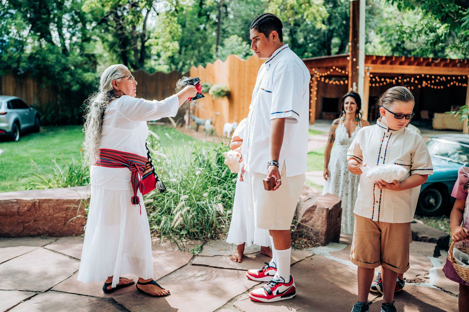 Casual outdoor gathering with people interacting on a stone patio surrounded by gardens.