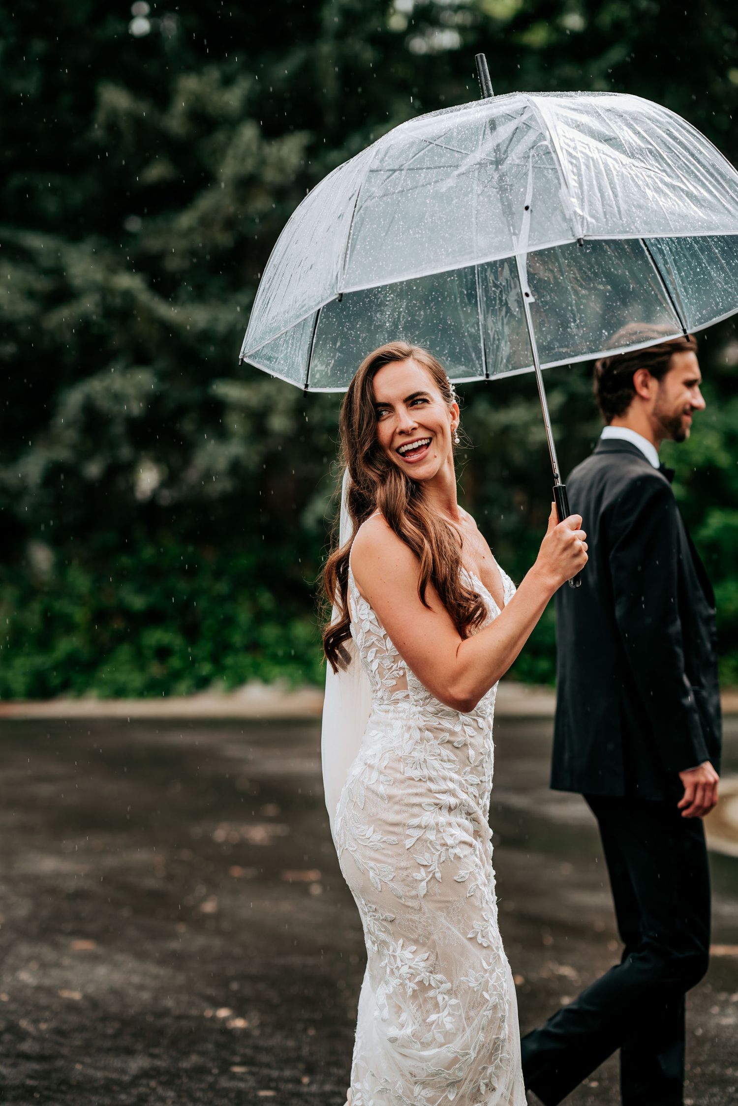 A bride holds a clear umbrella while smiling on a rainy wedding day.