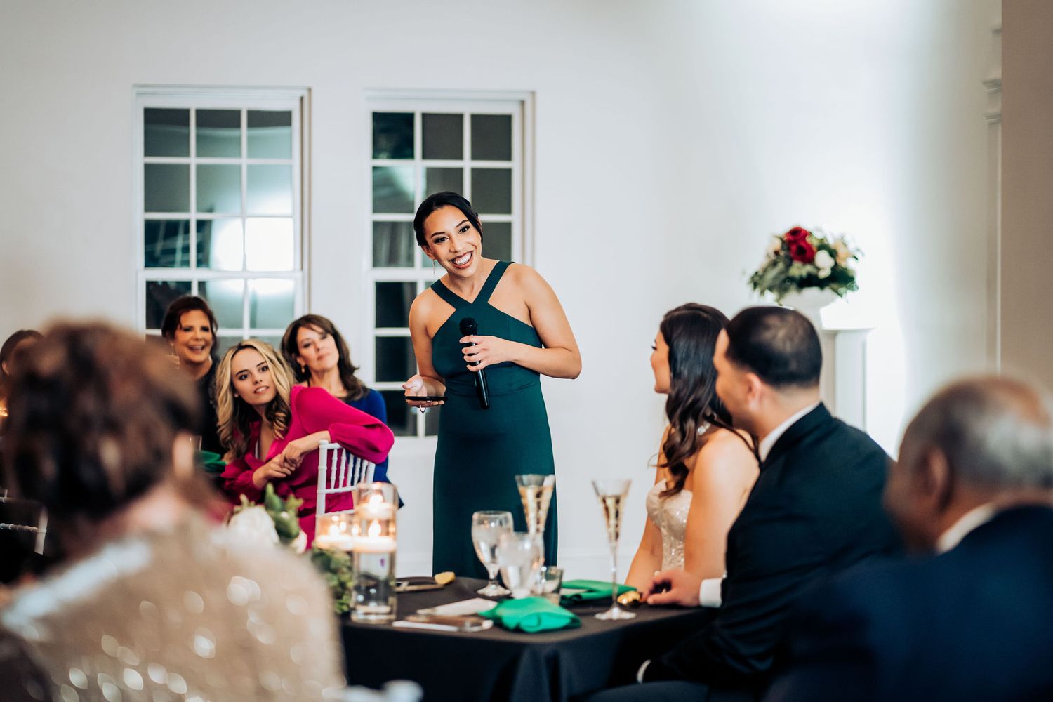 Wedding reception speaker addressing guests at an elegant indoor celebration with decorated tables.