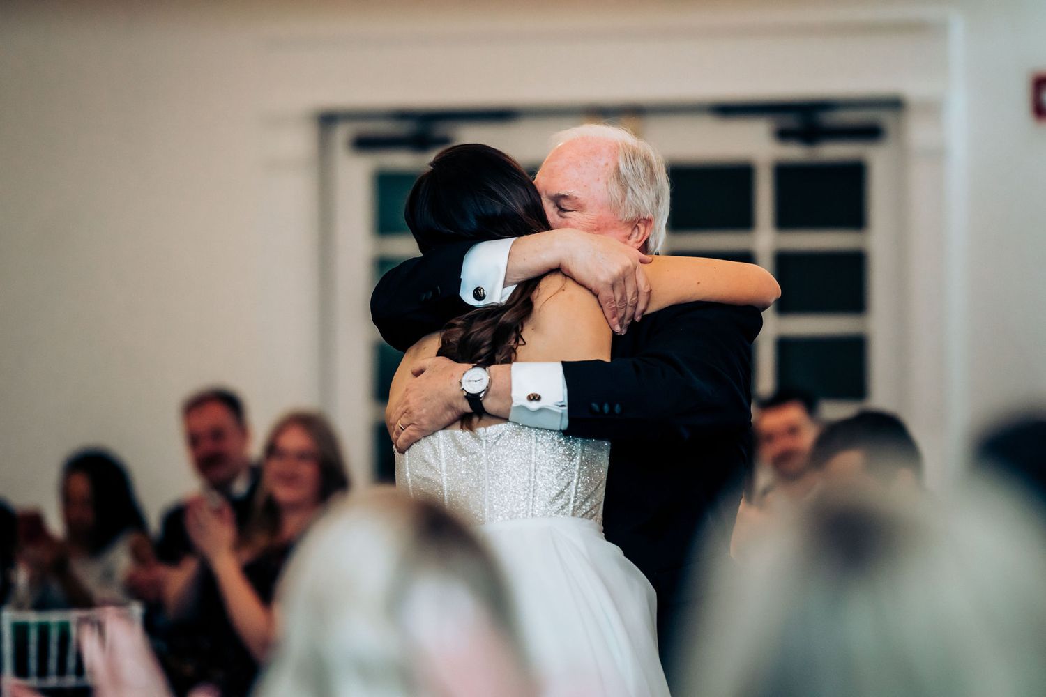 Emotional dance moment captured during wedding reception in elegant white venue.