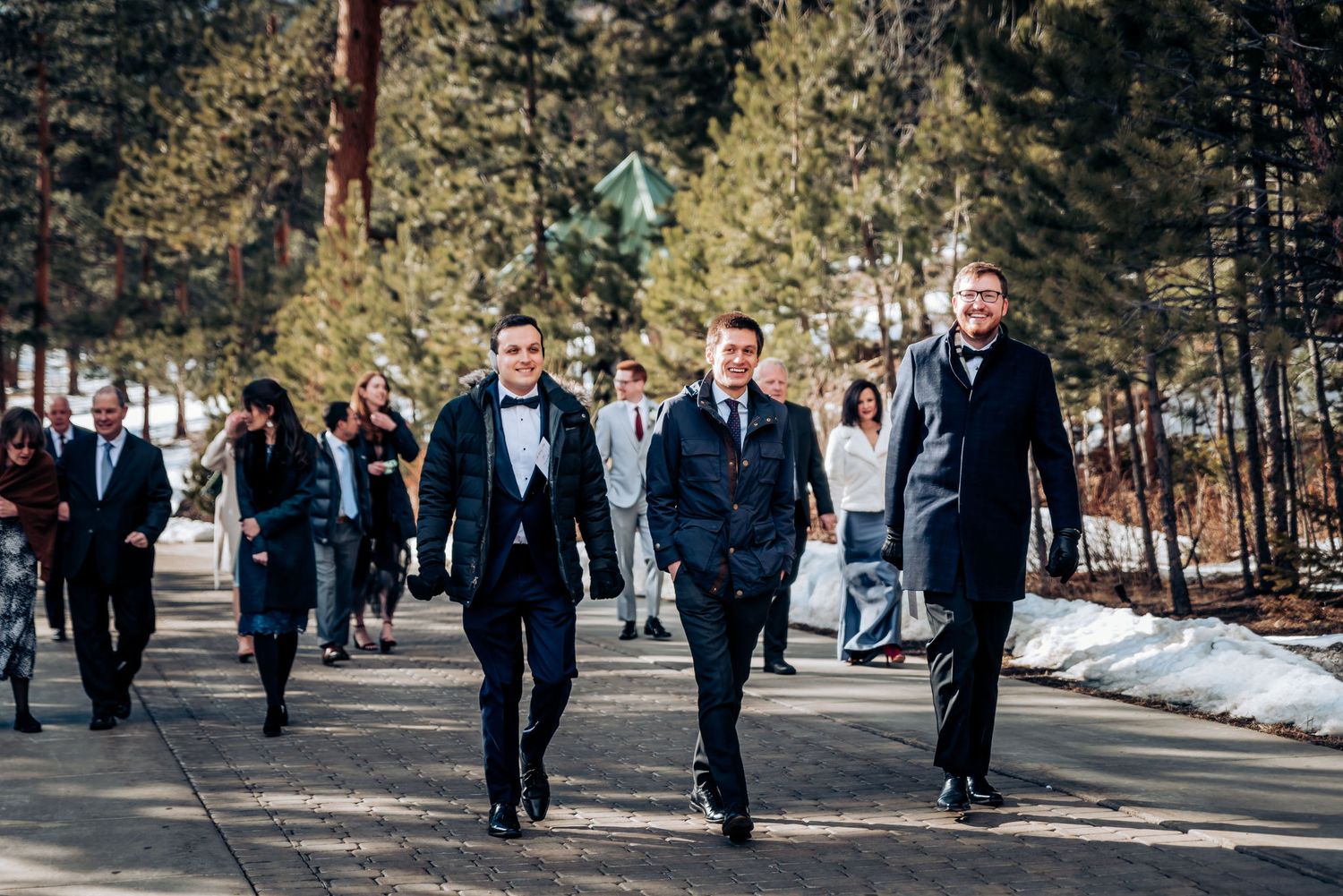 Groomsmen walking together outdoors in formal attire during winter wedding.