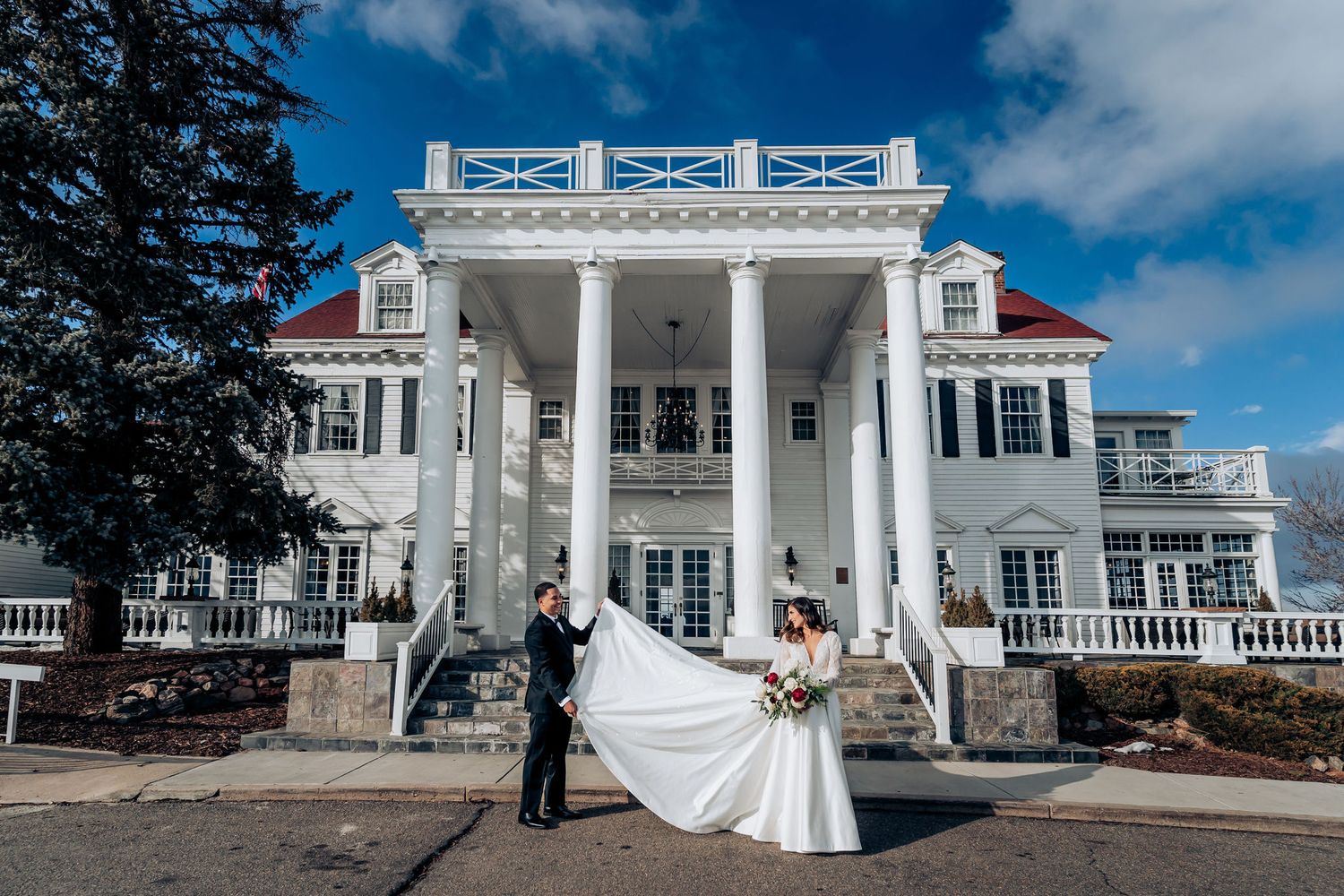 Elegant wedding portrait in front of grand white colonial mansion with columns.