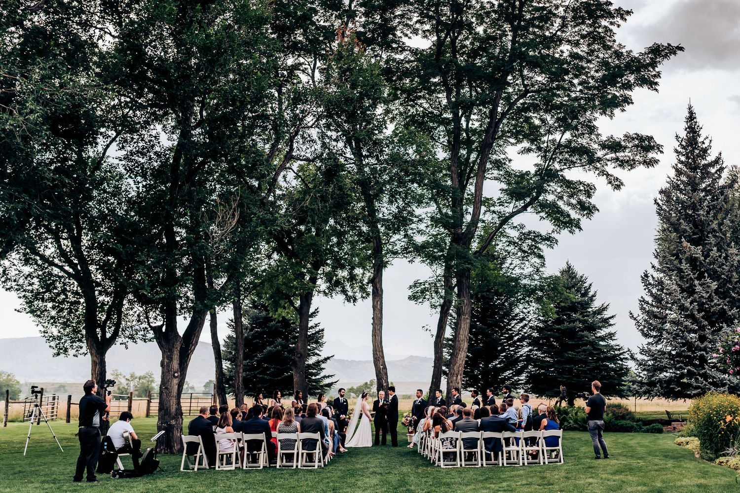 White chairs set up for outdoor wedding ceremony under tall trees with mountain views.