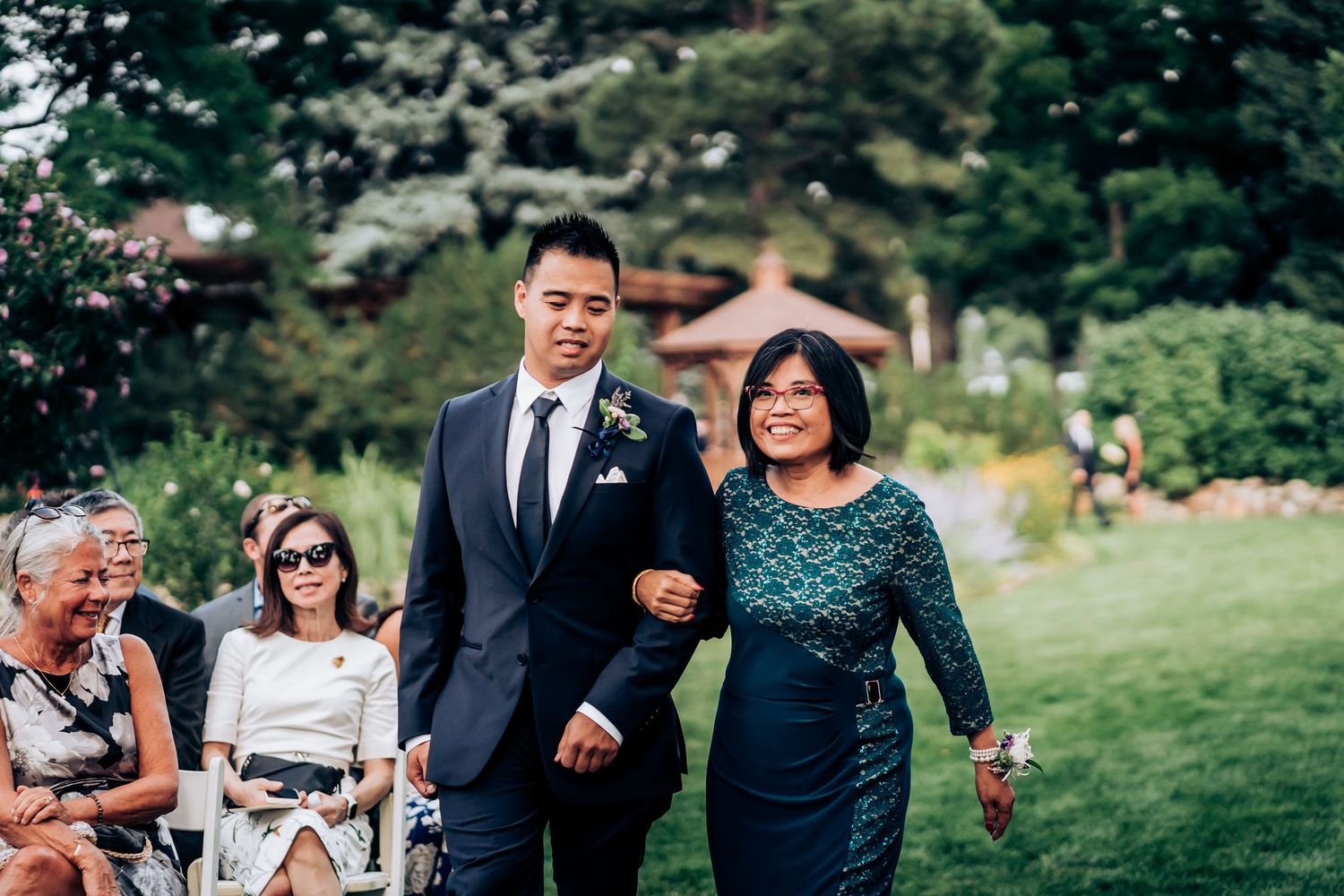 Wedding processional on a green lawn with guests seated in white chairs.