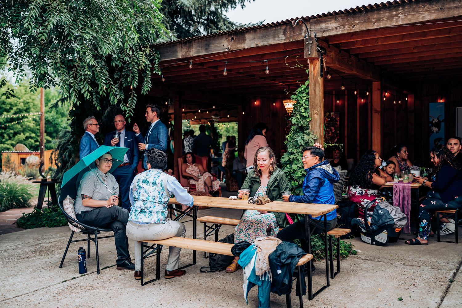 People gathered at rustic outdoor dining area with wooden benches under covered patio.