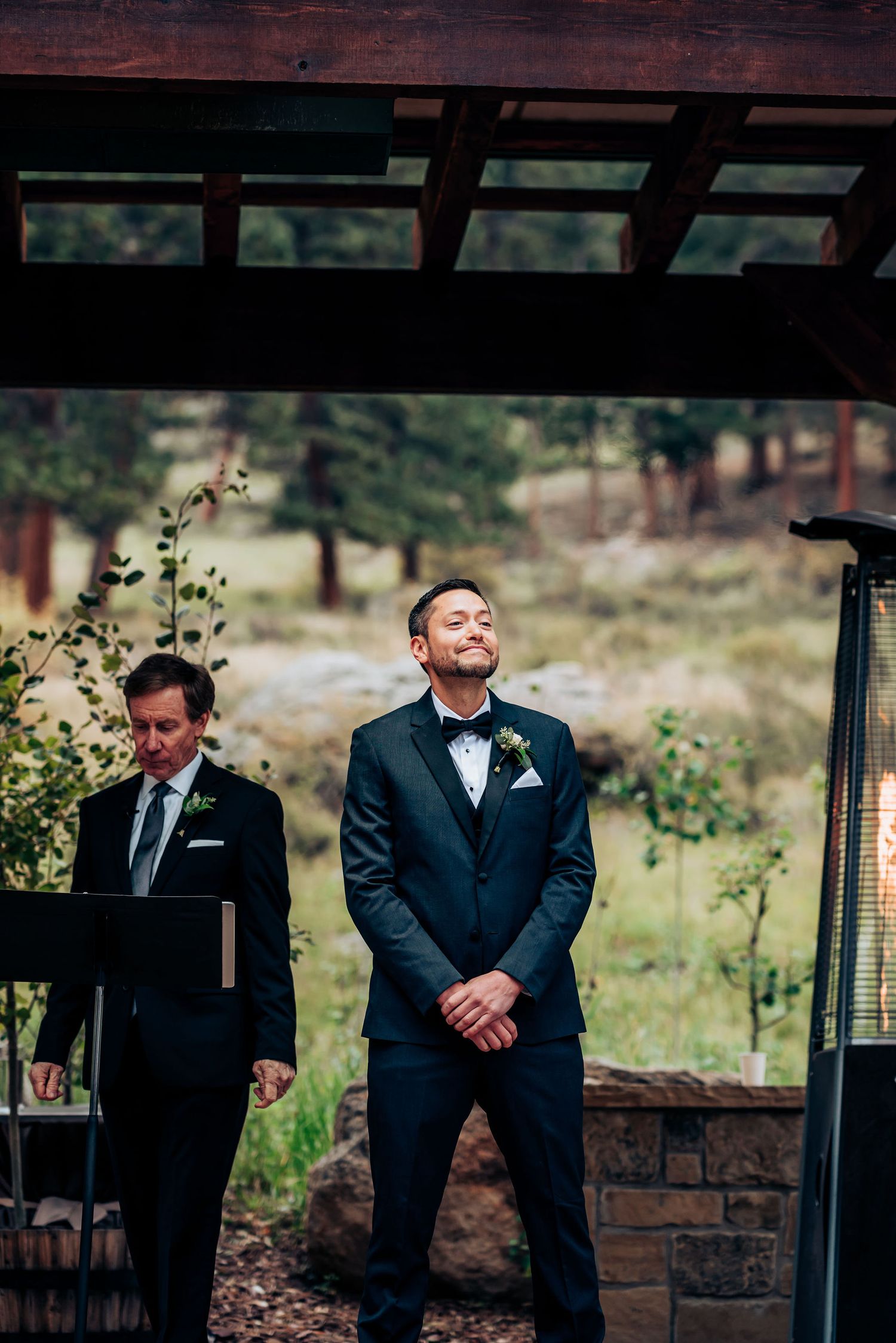Groomsmen standing under wooden pergola in mountain setting wearing formal suits.