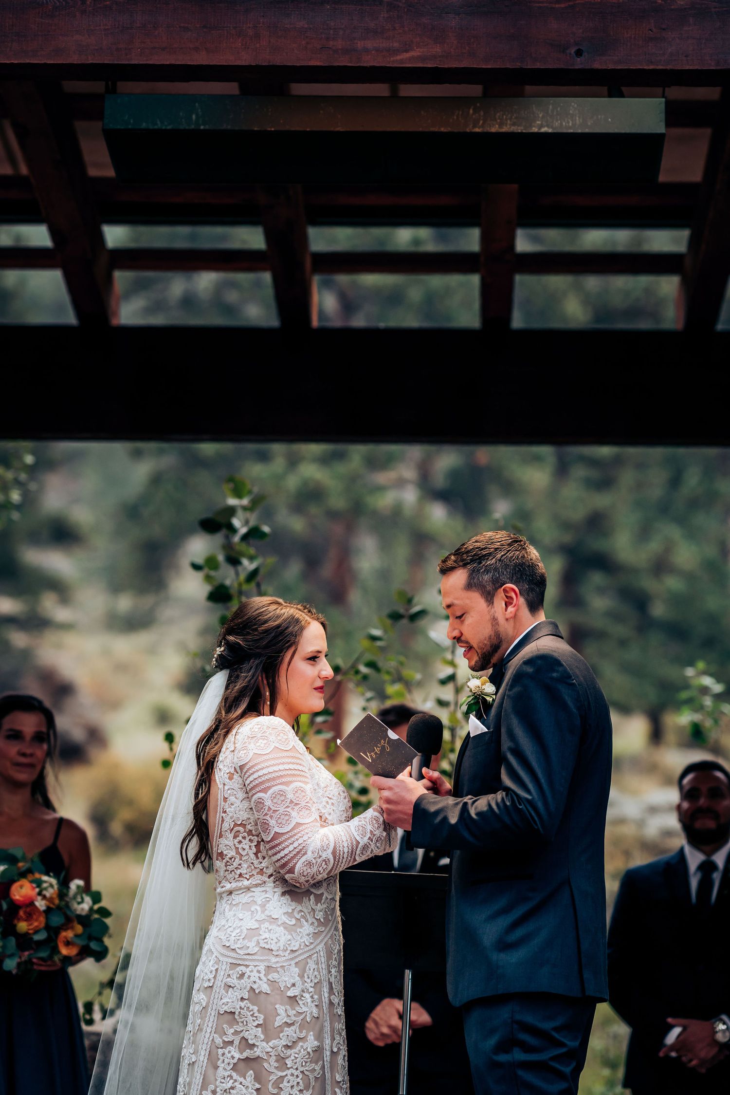 Emotional wedding ceremony exchange under rustic wooden pavilion with forest backdrop.