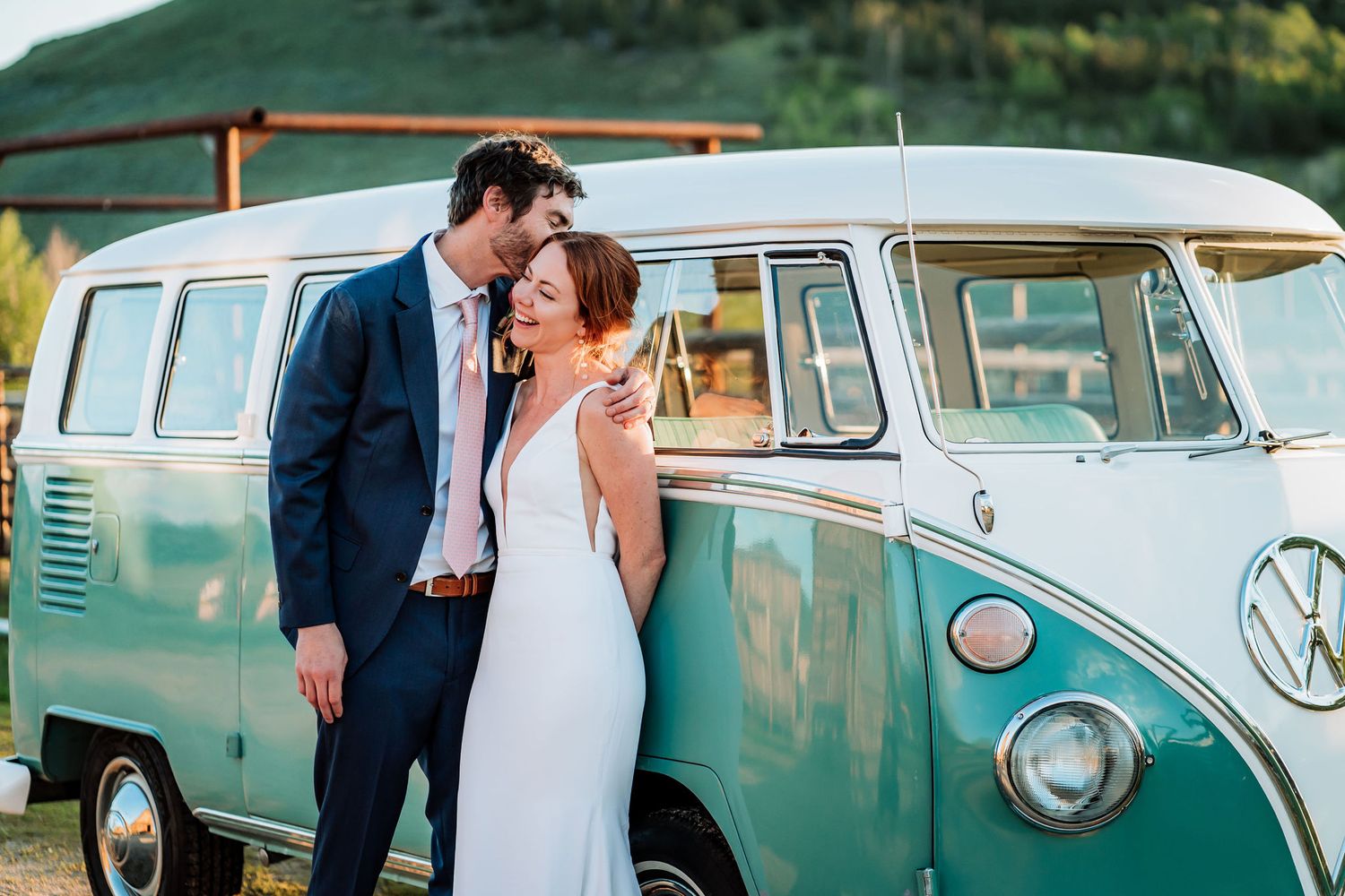 An elegant couple embraces next to a vintage turquoise and white Volkswagen microbus.