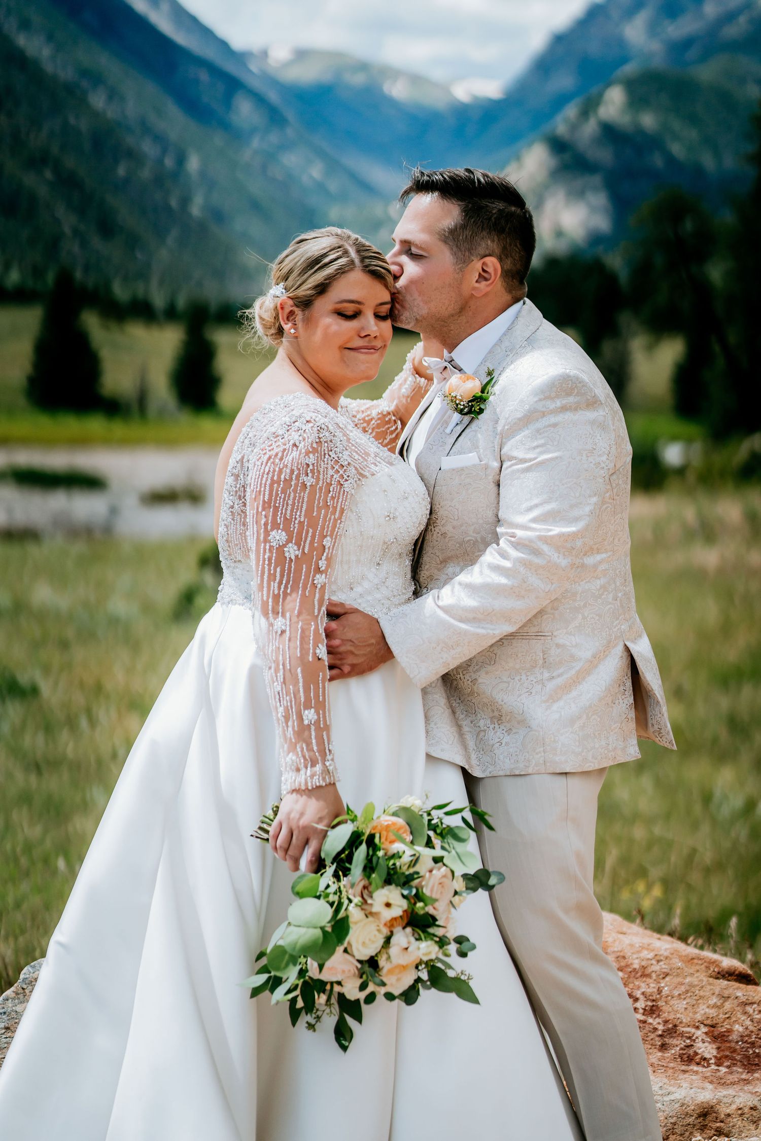 Wedding couple embraces in front of dramatic mountain valley landscape.