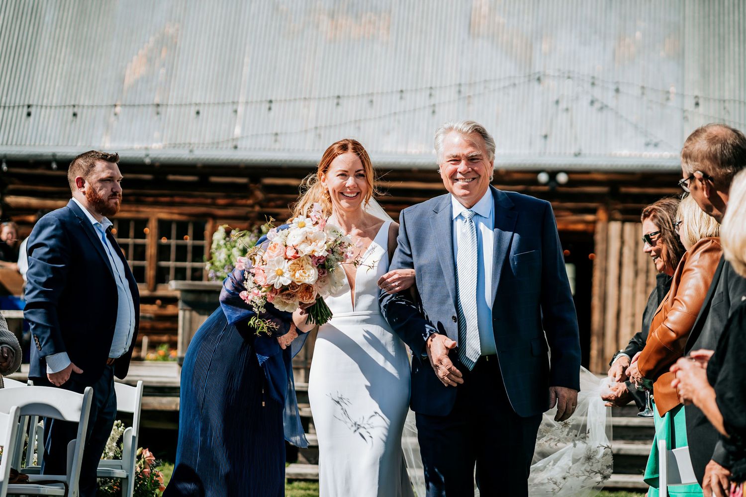 Wedding party exits rustic barn venue during outdoor mountain ceremony.