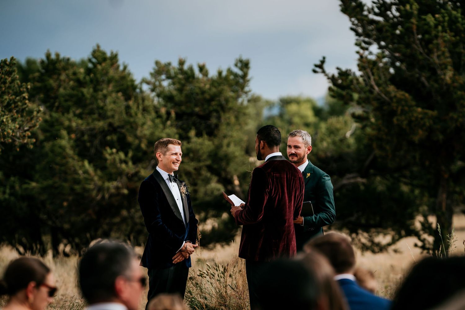 Small outdoor wedding gathering surrounded by pine trees and natural landscape.