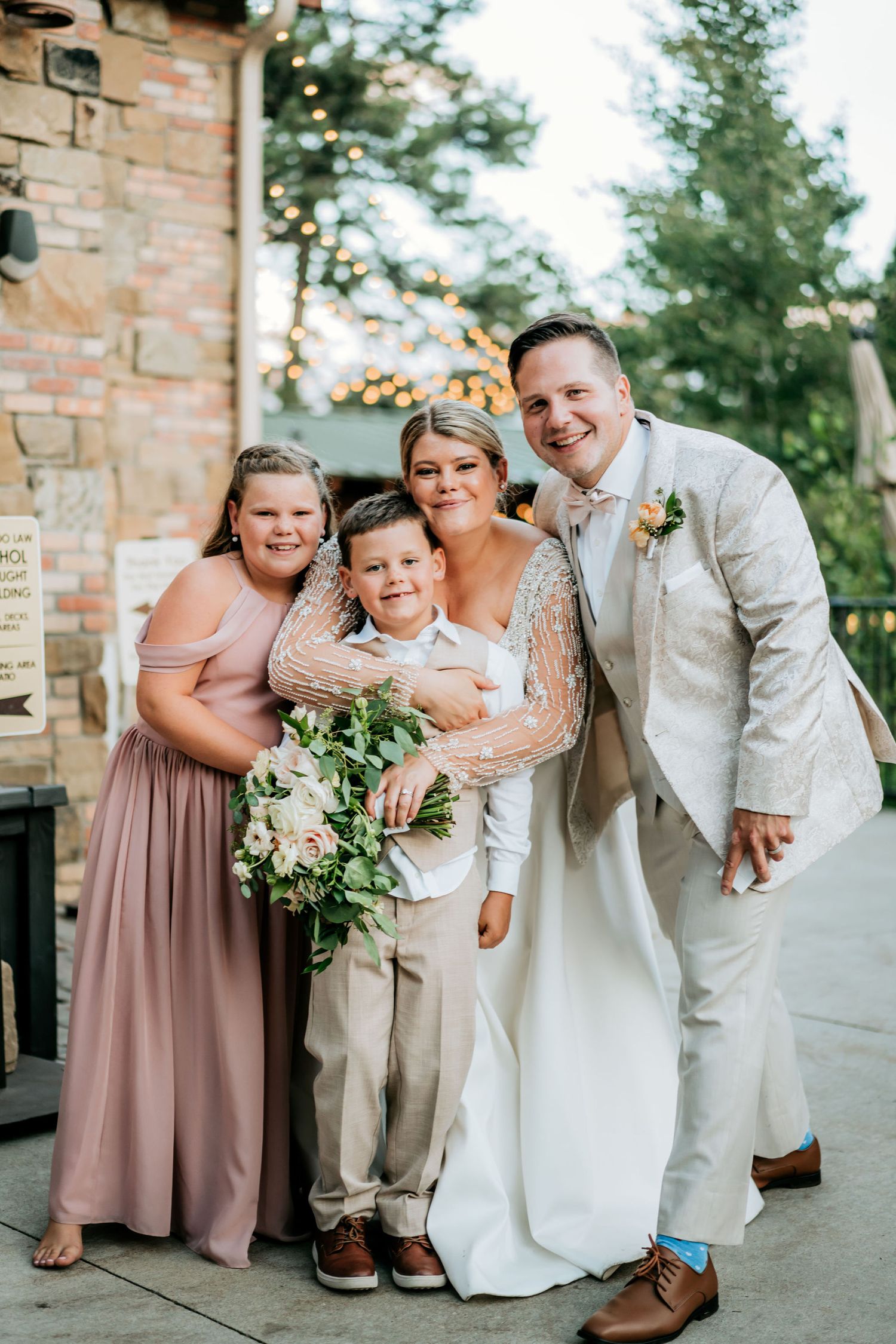 Family portrait at outdoor wedding venue with brick wall and greenery.