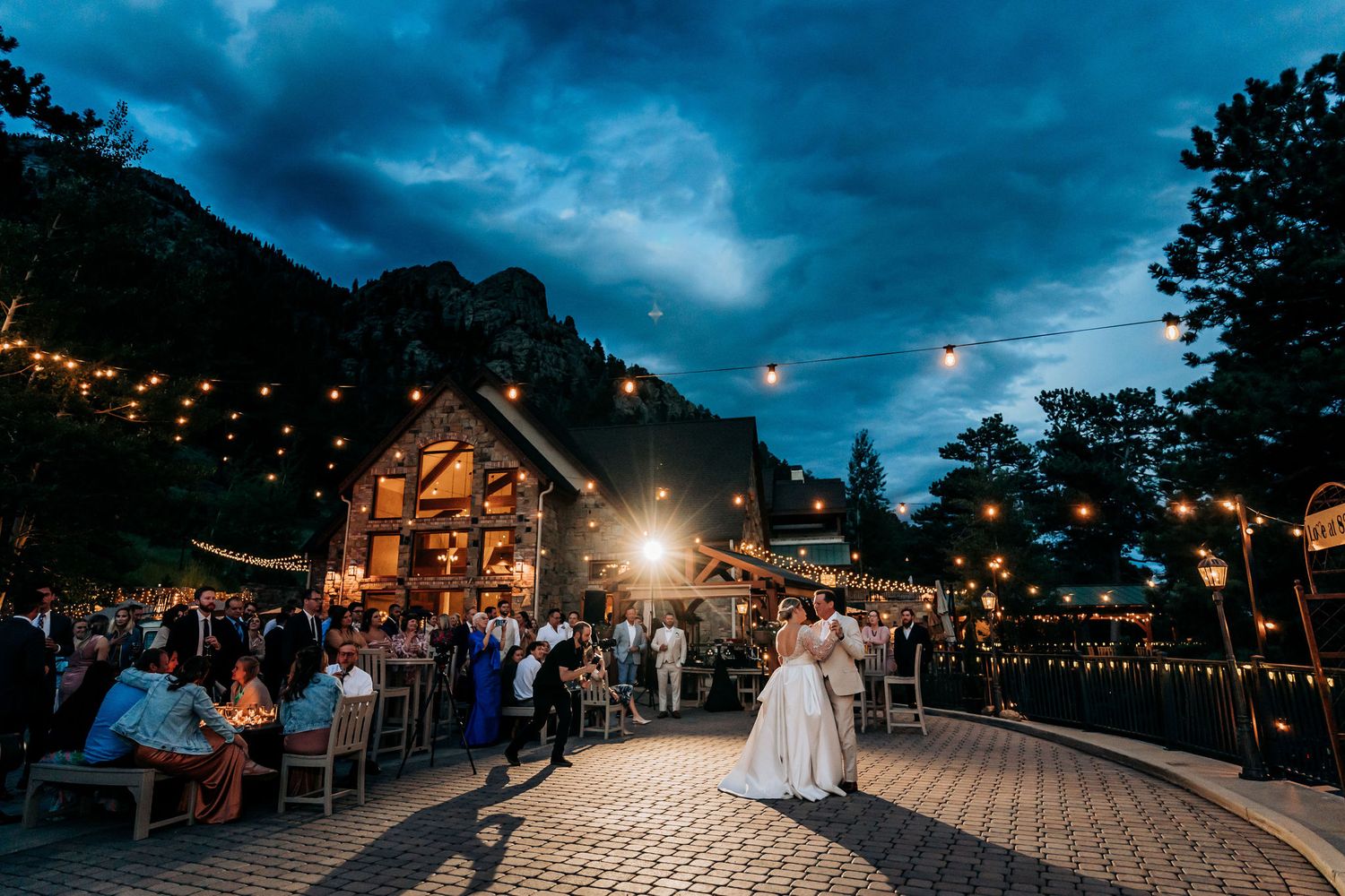 Evening wedding reception at a rustic barn venue with string lights under dramatic blue skies.