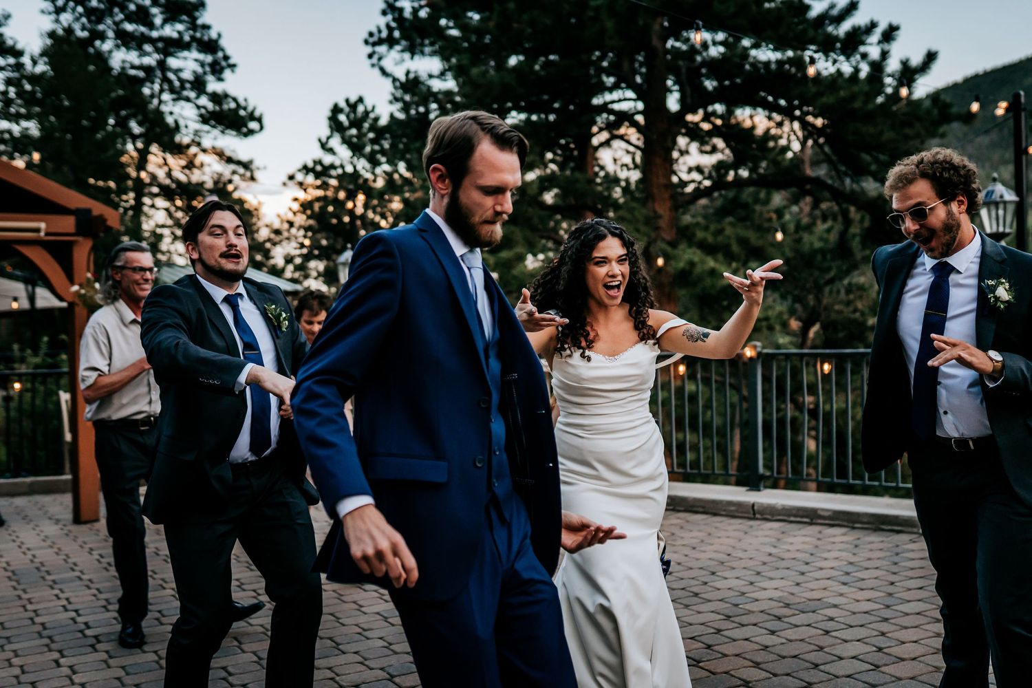 Wedding reception dance party with guests celebrating under string lights outdoors.