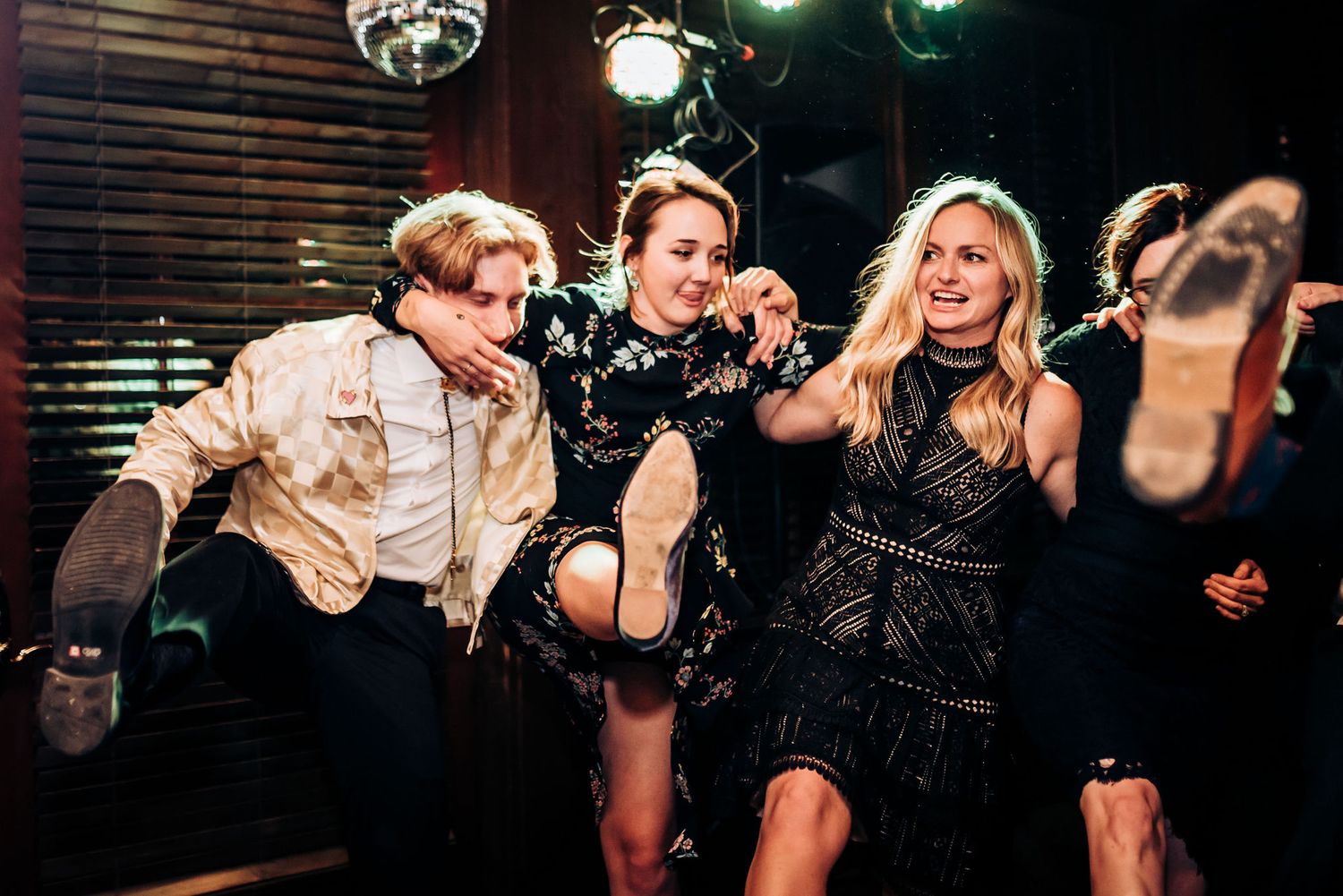 Party guests dancing wildly in formal attire under disco lights.