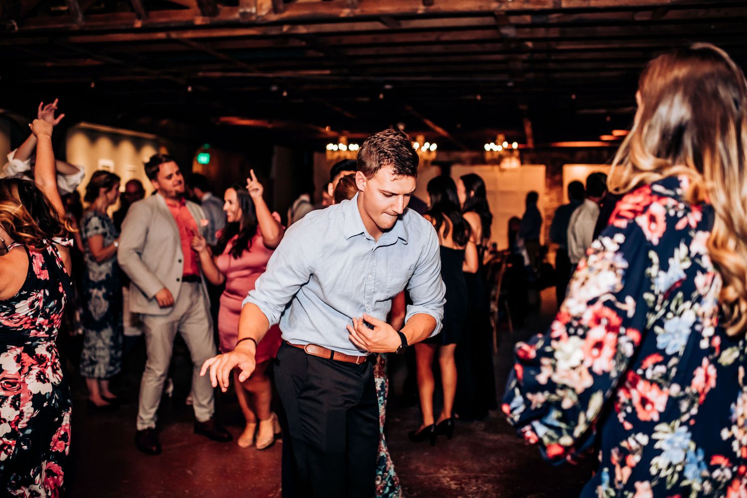 Wedding guests dancing and having fun at a reception with string lights and rustic decor.