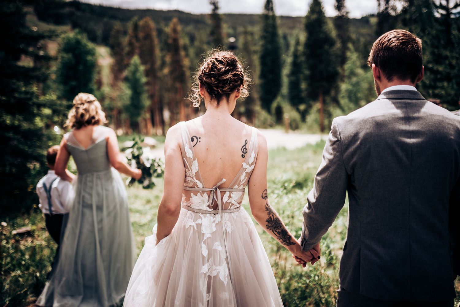 Back view of bridal party walking through mountain meadow with lace dress details and florals.