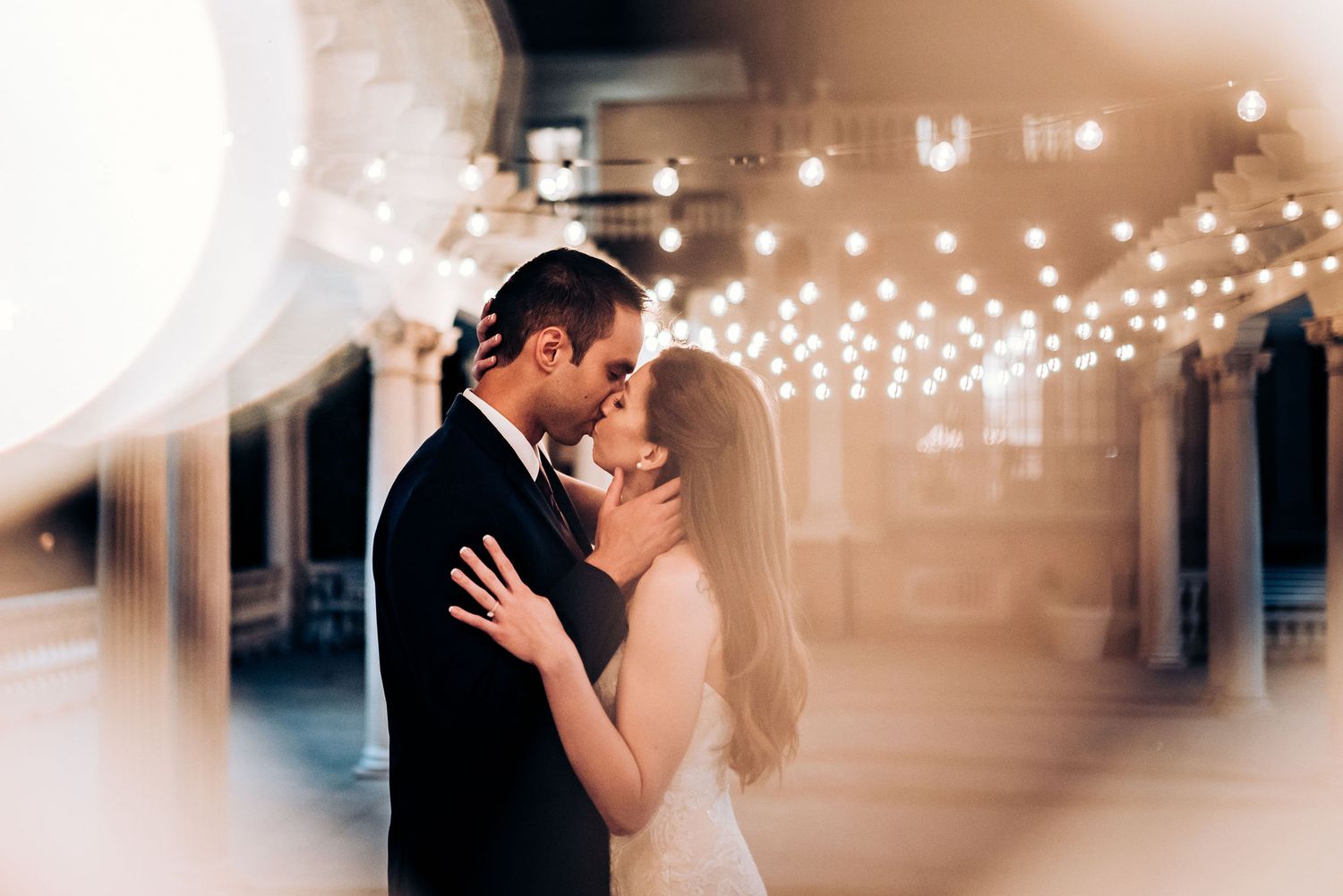A romantic wedding moment captured through soft focus with string lights creating a dreamy atmosphere.