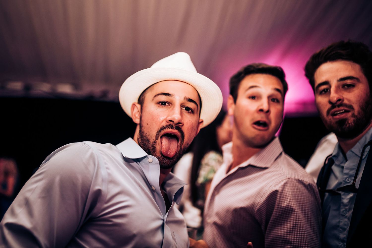 Three party guests make animated expressions at a wedding reception.