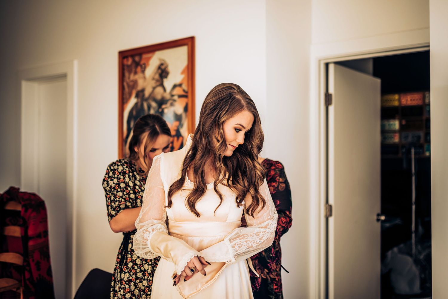 A tender moment during wedding preparations in a room with warm lighting and artwork.