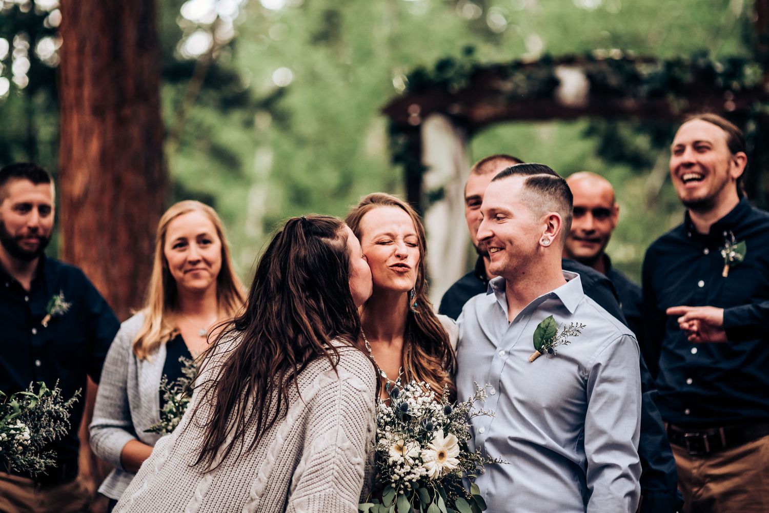 Candid moment of celebration among wedding party members in wooded outdoor setting.